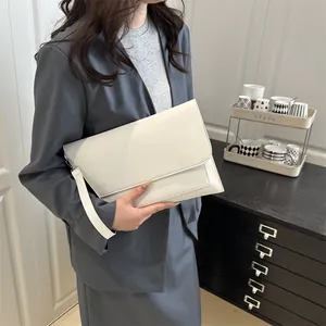 Pochette enveloppe minimaliste en cuir blanc crème portée par un mannequin en costume gris