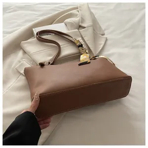 Detail of a brown leather tote bag with a decorative floral silk scarf on the handle