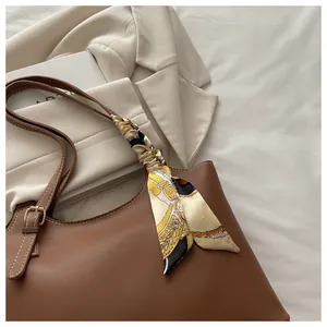 Close-up of brown leather tote bag handle decorated with a vintage pattern silk scarf