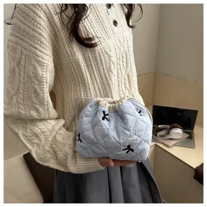 Detail of light blue quilted drawstring bag with elegant black bow embroidery and texture