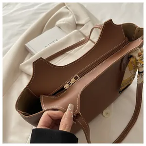 Brown tote bag detail with white stitching, gold zipper closure and silk scarf decoration