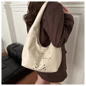 Détail du sac hobo crème avec des rivets argentés en forme d'étoile porté par un mannequin