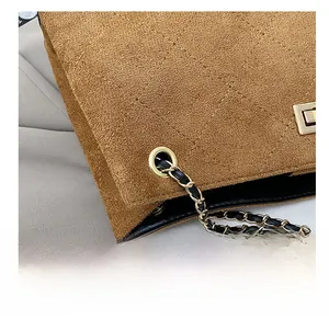 Détail macro des anneaux dorés et de la bandoulière en chaîne sur un sac en daim marron