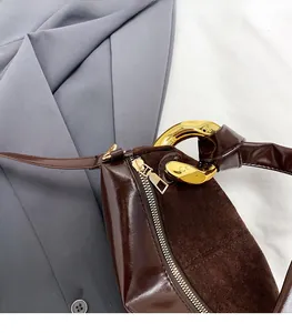 Detail of dark brown suede shoulder bag with polished gold zipper and chain accents