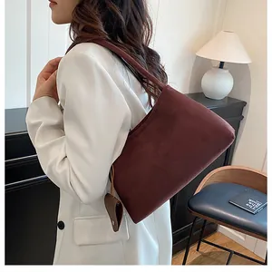Deep burgundy suede underarm bag shown as worn by model in an elegant interior setting