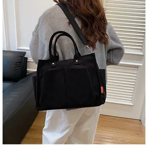 Vista laterale della borsa tote in velluto a coste nero con tasche e tracolla in tessuto