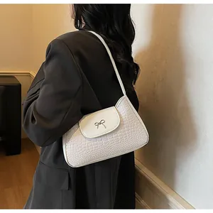 Vue détaillée d'un sac porté épaule blanc texture croco avec un nœud argenté sur un mannequin