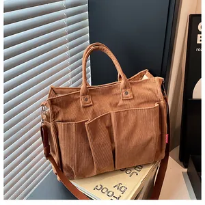 Dettaglio borsa a tracolla in velluto marrone con tasche frontali ed etichetta rossa