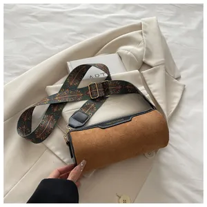 Detail der matten braunen Zylindertasche mit Ethno-Gurt auf weißem Blazer
