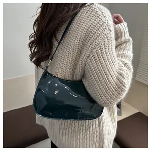 Close-up of a dark green patent leather shoulder bag with a metallic gold zipper detail