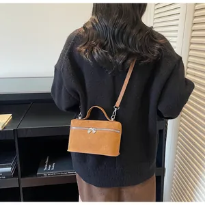 Detail of a brown matte suede box bag with heart zipper pull shown in a lifestyle setting