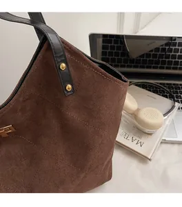 Close-up of large brown suede tote bag with black leather strap and gold rivet details