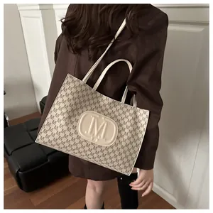 Detail of trendy beige tote bag with M-pattern and large embossed logo worn by model