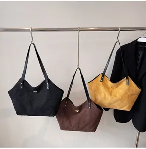 Detailed view of three suede tote bags in black, brown, and ginger with gold turn-lock hardware