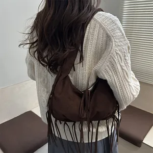 Grand sac hobo en daim marron foncé avec franges porté à l'épaule dans un décor intérieur