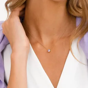 Detailed view of a dainty gold necklace with a round purple birthstone on a model