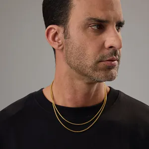 Gros plan de deux colliers à chaîne box dorés vintage superposés sur un pull noir