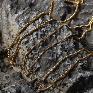 Détail de colliers chaîne box dorés vintage superposés sur un fond de roche texturée