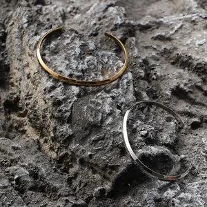 Detail of minimalist geometric gold and silver bangles with faceted edges on rock background