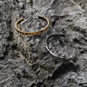 Detailed view of polished gold and silver stainless steel open cuff bracelets on dark stone