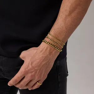 Dettaglio di tre bracciali a catena cubana dorata e un anello sul polso di un uomo