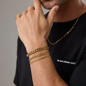 Primo piano di tre bracciali a catena cubana dorata di diverse larghezze sul polso maschile