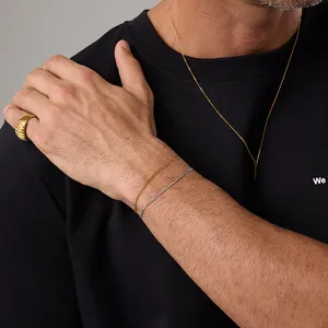 Close-up of a man wearing an 18K gold Cuban link bracelet and minimal jewelry stack