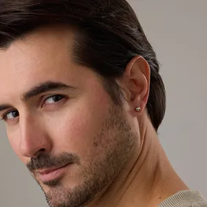 Macro detail of minimalist silver ball stud earring on male model showing polished finish