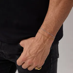 Close-up of gold and silver slim curb chain bracelets and minimalist gold wide band ring