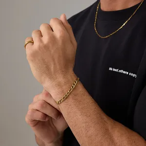 Détail d'un bracelet Figaro doré et d'une bague polie portés par un mannequin en noir
