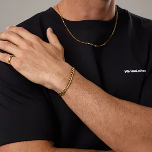 Gros plan sur l'ensemble bracelet Figaro et bague dorée sur fond de chemise noire