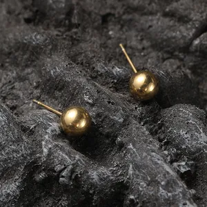Detailed view of polished gold ball stud earrings on a dark textured stone background