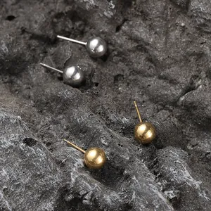 Close-up of minimalist gold and silver ball stud earrings on a black rock surface