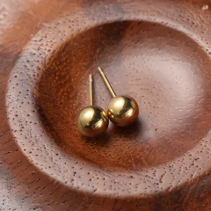 Macro shot of minimalist gold round bead earrings on natural dark wood texture