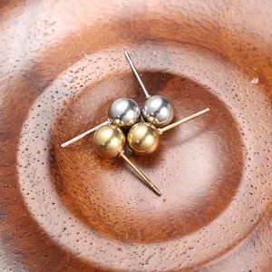 Close-up of gold and silver ball stud earrings on a natural wood textured surface