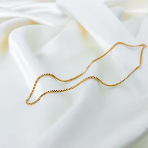 Elegant gold box chain necklace displayed on white silk fabric, minimalist jewelry style