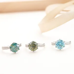 Detailed macro of three round-cut moissanite rings in green and blue on a silk ribbon