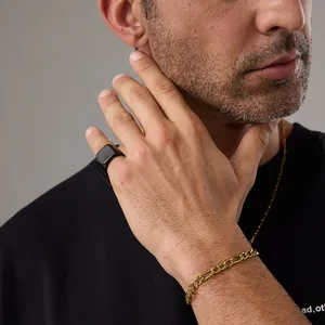 Detail of a matte black signet ring and a gold Figaro chain bracelet on a male model