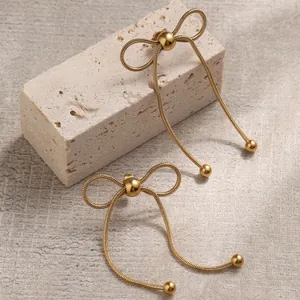 Elegant gold bow earrings with snake chain tassels and bead accents on stone surface