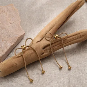 Detail of gold bow tassel earrings with snake chain and beads on wooden branch