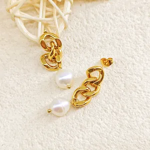 Détail des boucles d'oreilles à chaîne dorée avec perles blanches sur fond texturé