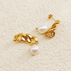 Détail de boucles d'oreilles chaîne dorée avec grandes perles baroques sur fond texturé