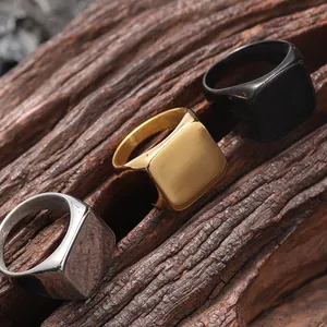 Detailed view of silver, gold, and black square signet rings on a textured wood surface