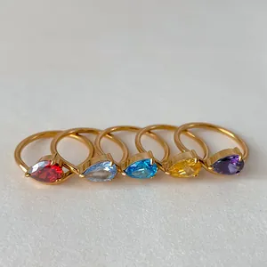 Close-up of five gold rings featuring colorful pear-cut gemstones in a minimalist design