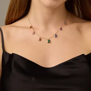Macro detail of gold necklace featuring colorful rectangular gemstones on a female model
