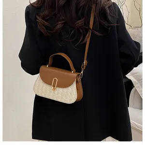 Detail of a chic straw crossbody bag featuring brown leather trim and a gold oval metal clasp
