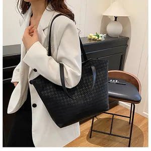 Detail of black tote bag with houndstooth texture and leather handles on model shoulder