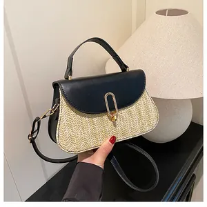 Detail of woven straw handbag featuring black leather trim and a golden oval metal clasp