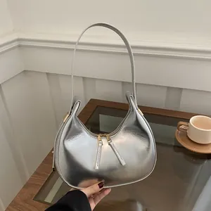 Detailed close-up of a metallic silver crescent shoulder bag on a glass table surface