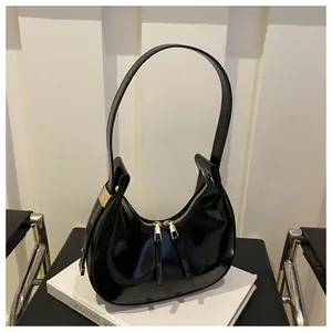 Detail of black patent leather crescent shoulder bag with golden metallic hardware